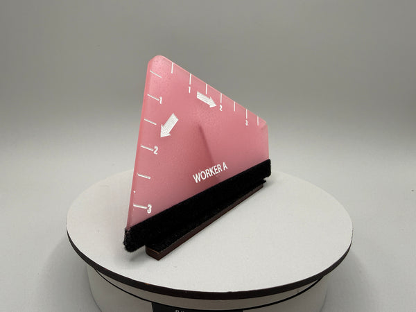 Pink triangular ruler with black base on a white platform against a gray background